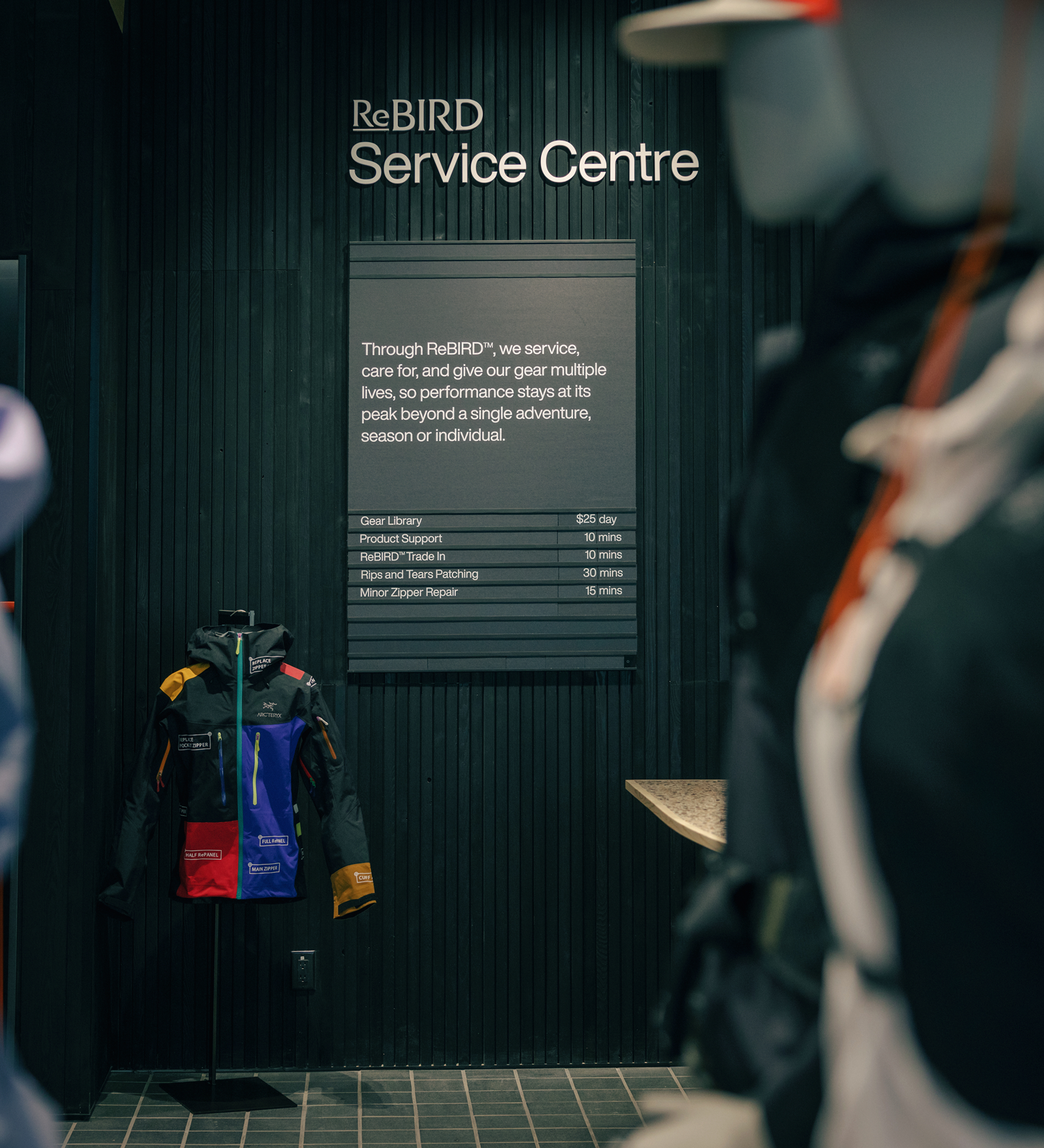 A dark wall with a "ReBIRD Service Centre" sign, a menu of gear repair and rental services, and a vibrant, multi-colored jacket on display.