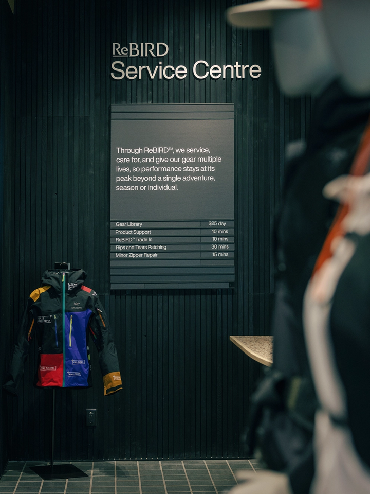 A dark wall with a "ReBIRD Service Centre" sign, a menu of gear repair and rental services, and a vibrant, multi-colored jacket on display.