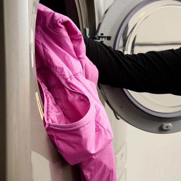 A person loads a pink jacket into a front-loading laundry machine.