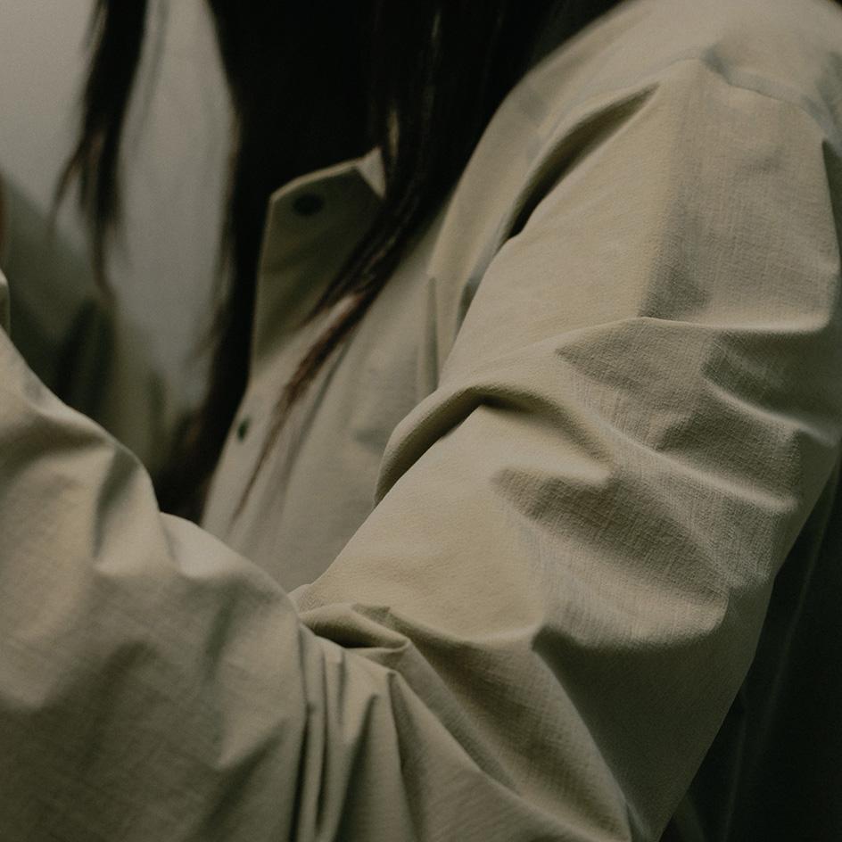 A person wearing a textured light olive shirt with visible folds.