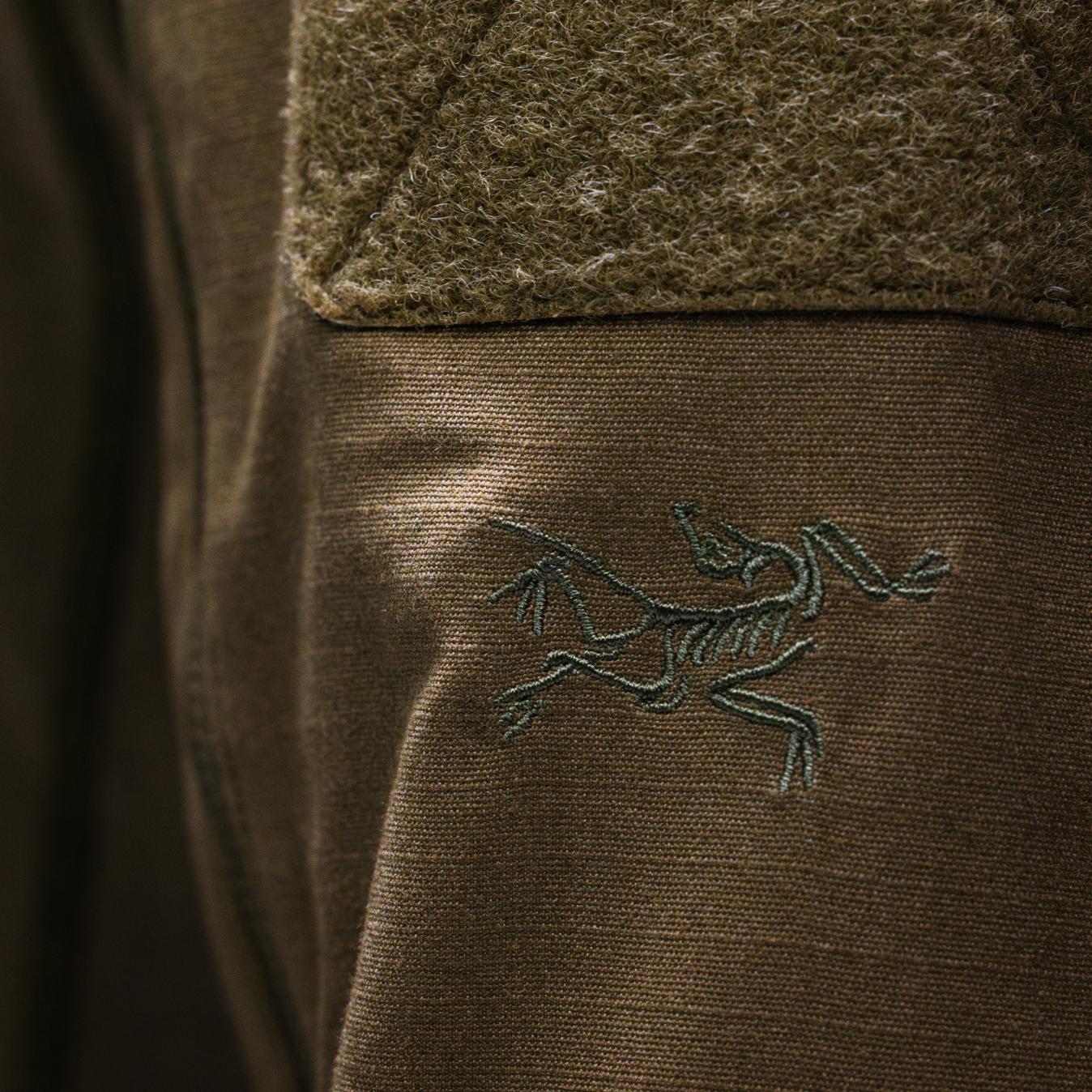 Embroidered Arc'teryx logo on olive green fabric with a textured green patch above it.