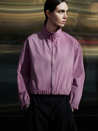 A woman wears a pink cropped jacket and black pants, looking right.