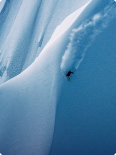 A skier carves down a steep, snow-covered slope, kicking up powder.