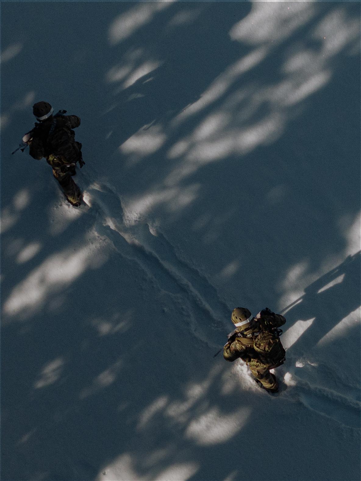 Overhead view of two soldiers walking through snow with dappled tree shadows.