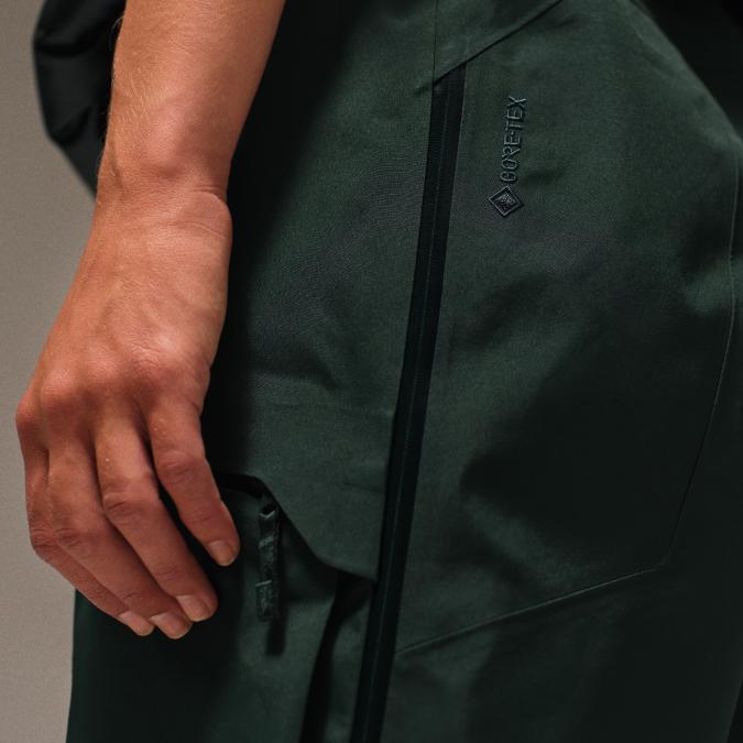 Close-up of a person's arm and hand next to a dark green Gore-Tex garment with a zipper.