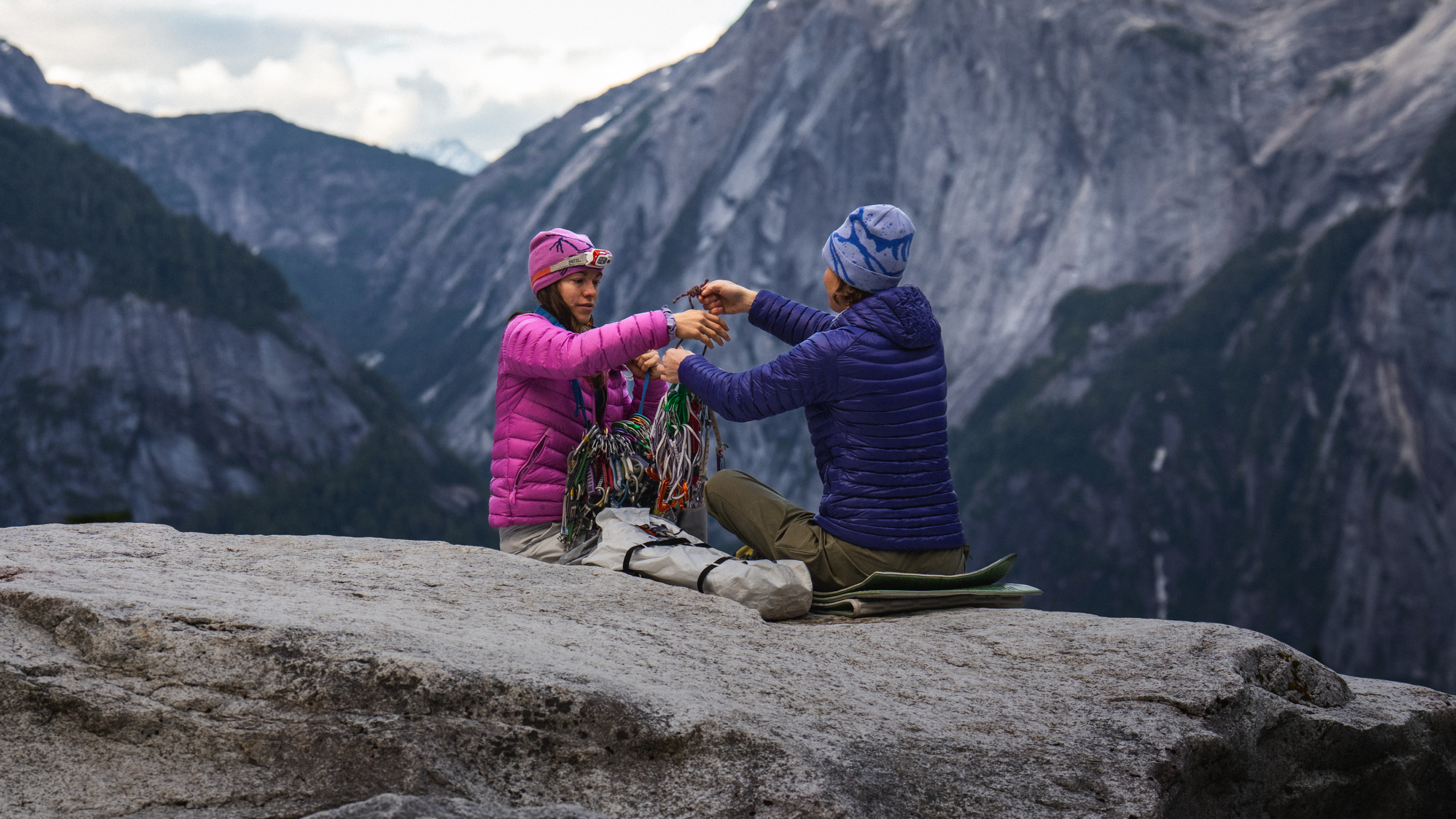 Two climbers organize gear on a rock in a mountainous landscape.