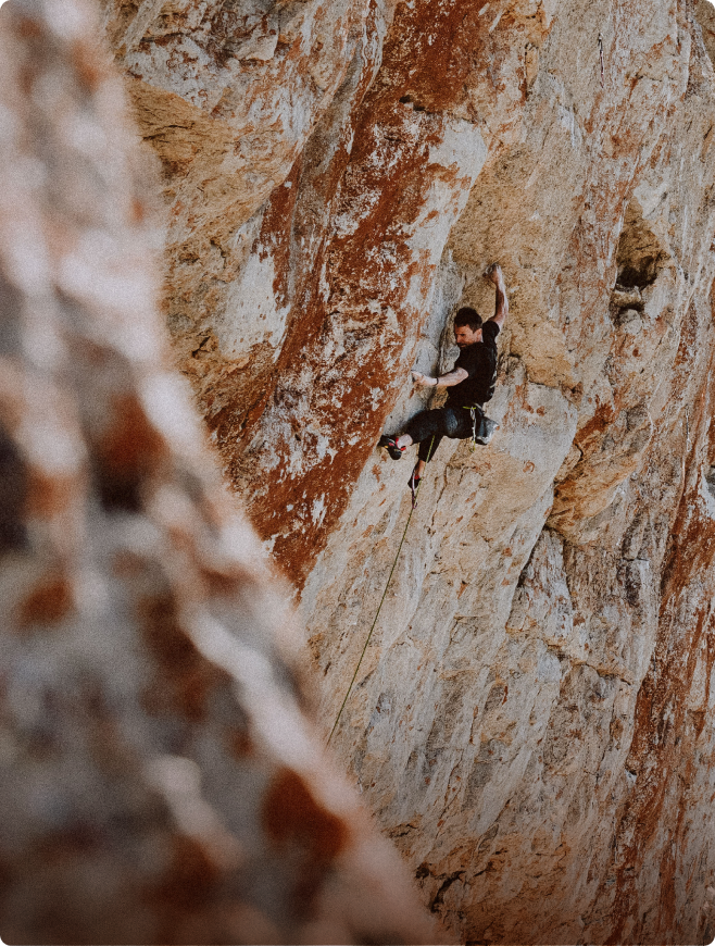A rock climber ascends a textured rock face, secured by a rope.