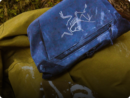 A dark blue bag featuring the Arc'teryx skeletal bird logo rests on an olive green fabric.