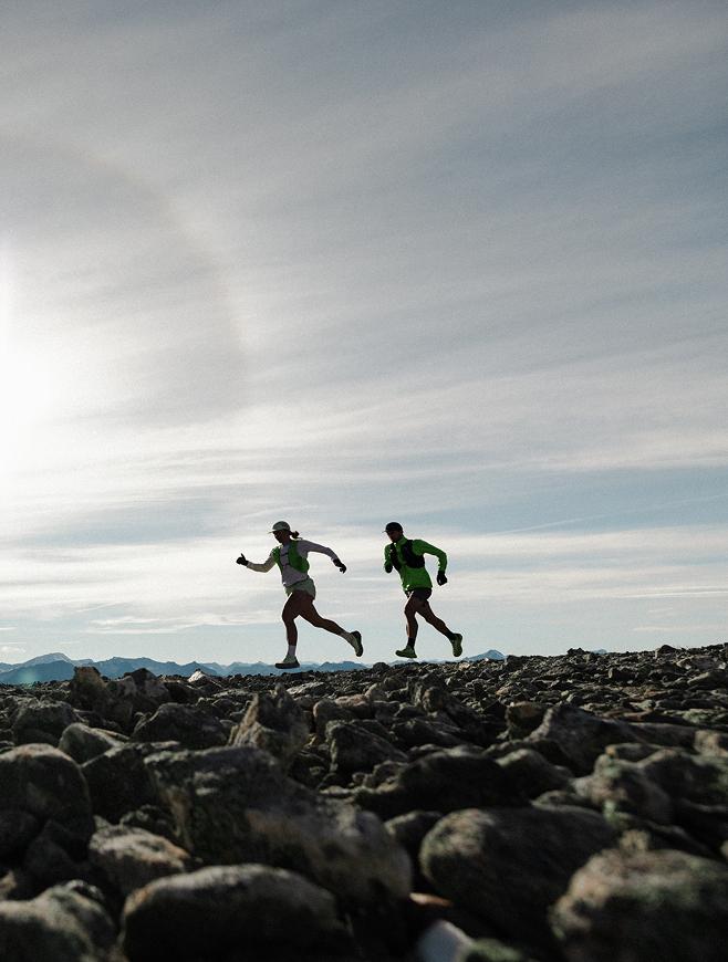 Two trail runners on a rocky landscape under a bright sky.