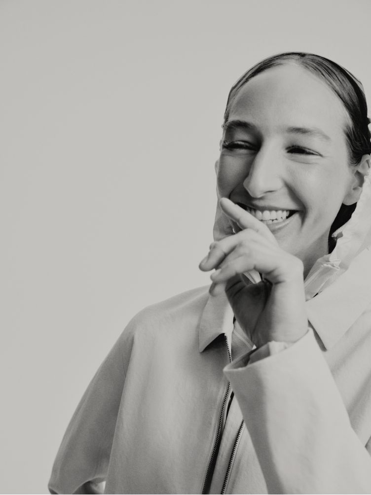 A black and white photo of a woman smiling broadly with her hand near her mouth.