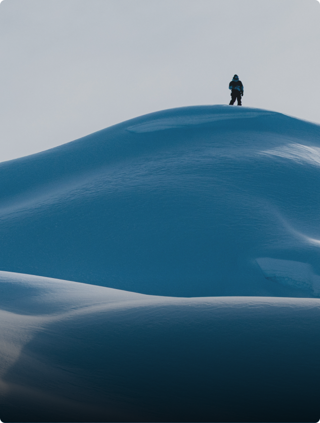 A person stands atop a snow dune against a pale sky.