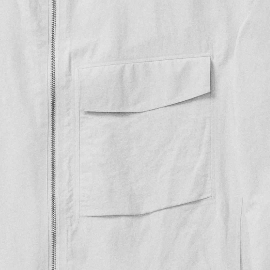 Close-up of a white garment with a zipper and two stacked flap pockets.