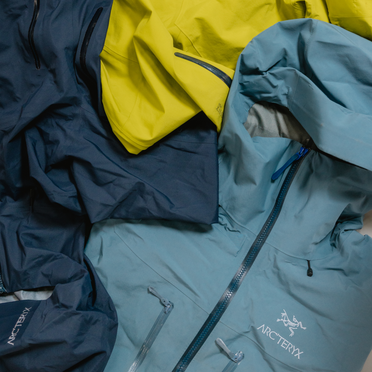 Three Arc'teryx outdoor jackets in blue, dark blue, and yellow.