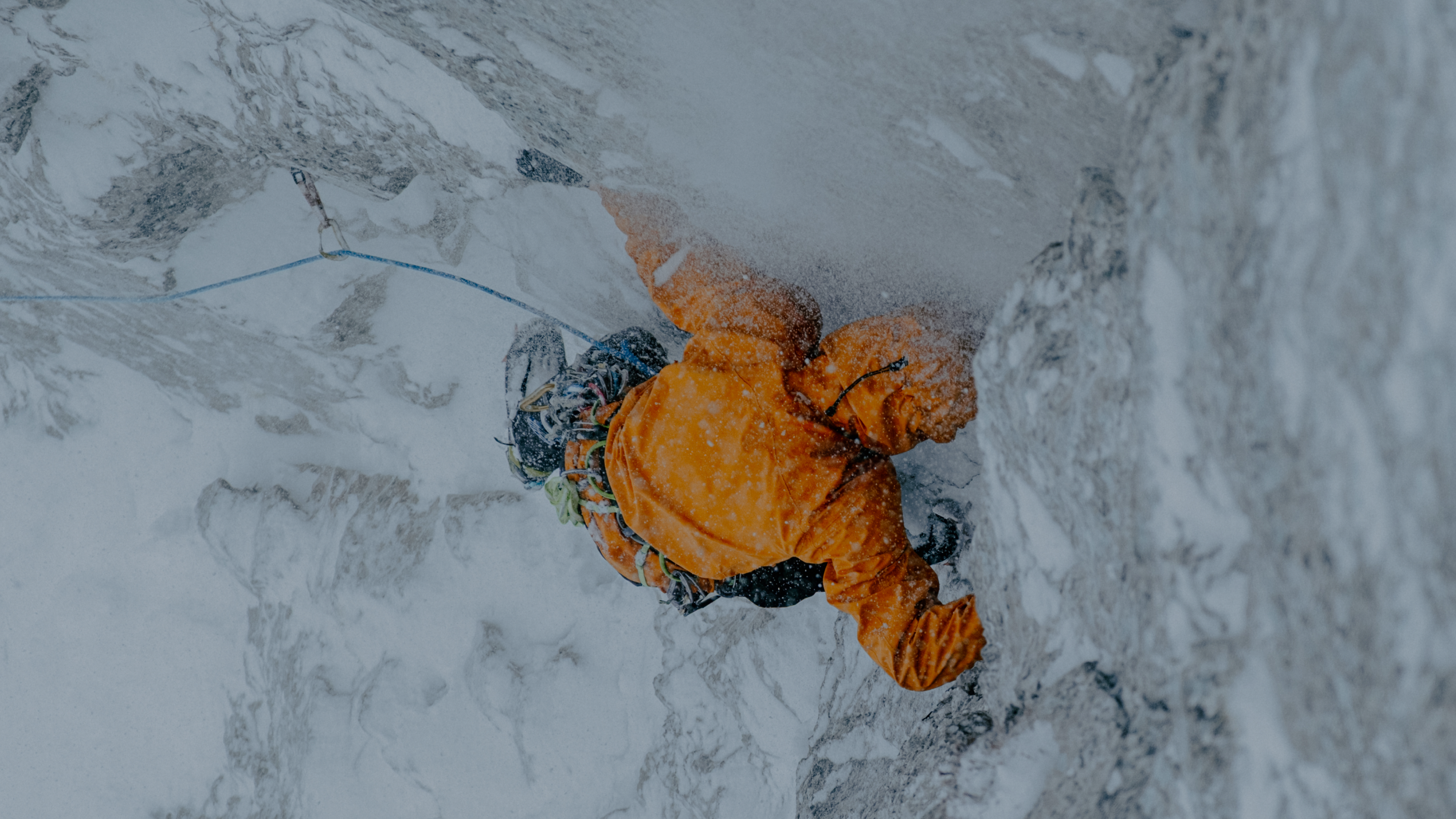 Person in a black ski helmet and goggles, wearing an orange jacket, surrounded by snow spray.