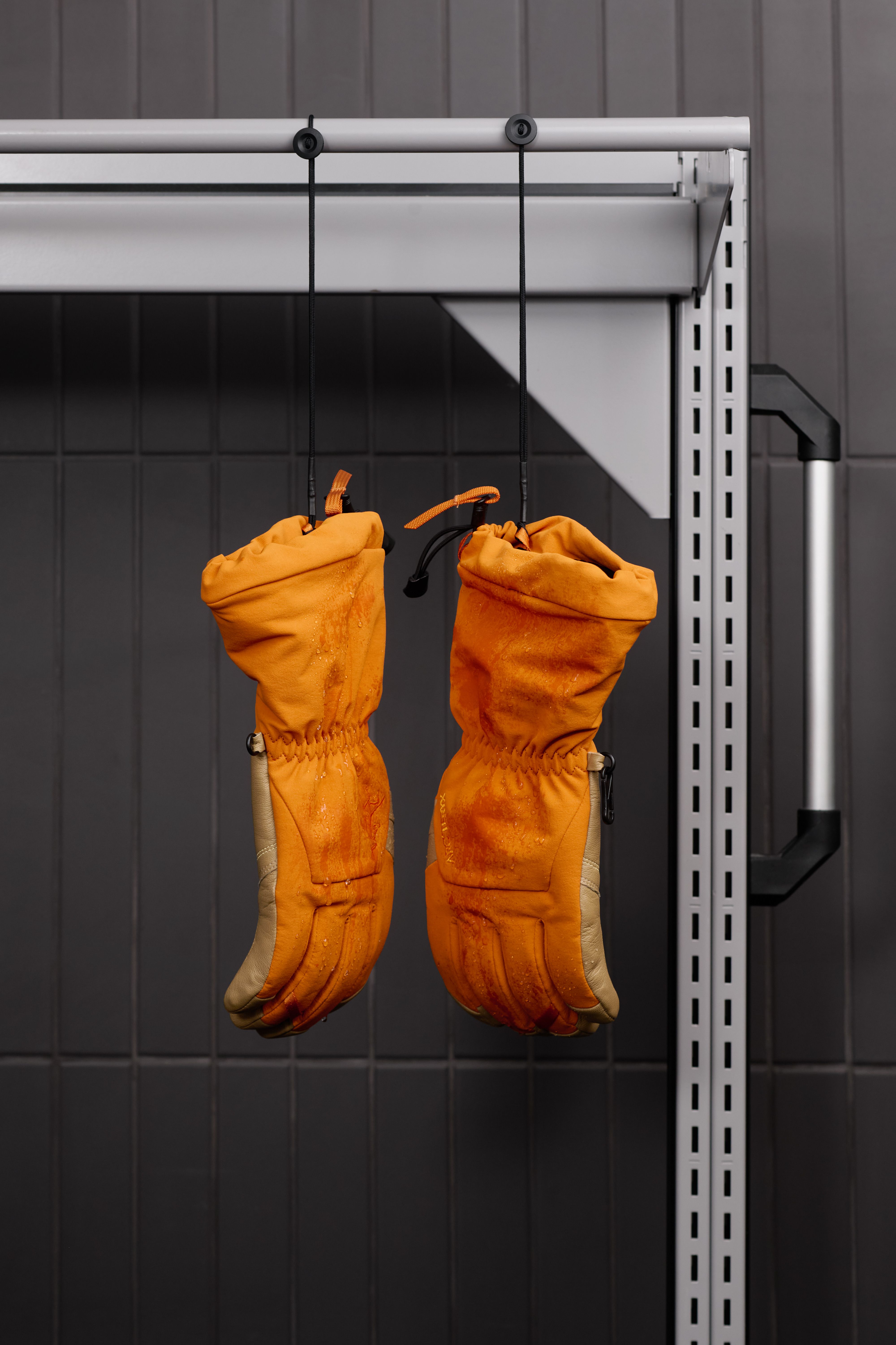 Wet orange and tan gloves hanging upside down from a rack.
