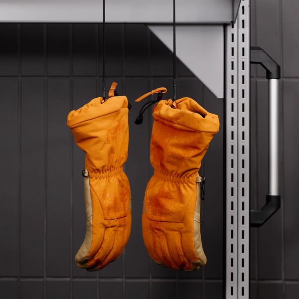 Wet orange and tan gloves hanging upside down from a rack.
