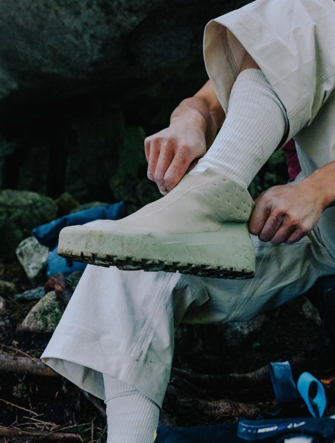 Hiker's leg in dark pants and a boot stepping on a rocky surface, hand gripping a rock.