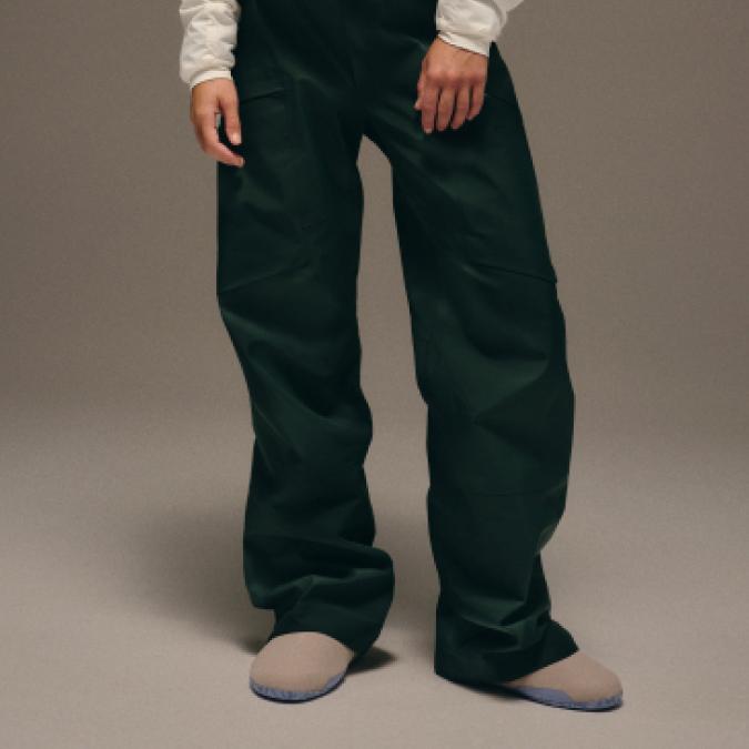 Person wearing dark green baggy pants and light beige slippers.