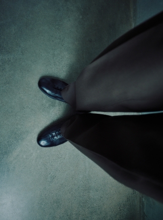 Top-down view of dark shoes and pants on a textured grey floor.