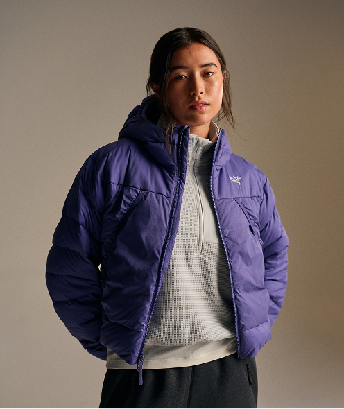 A woman wears a purple hooded Arc'teryx puffer jacket over a light grey half-zip top.