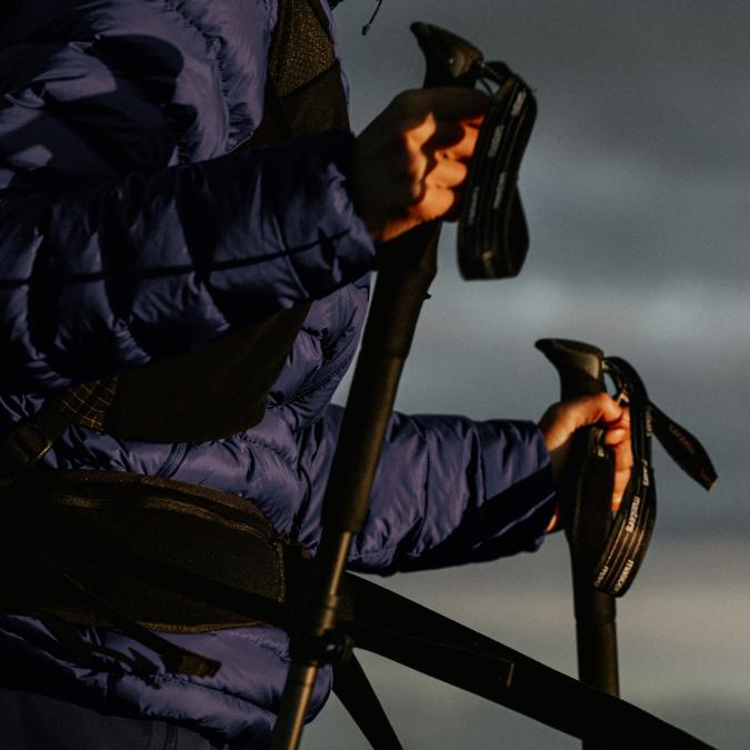 A person in a blue puffer jacket holds two trekking poles.