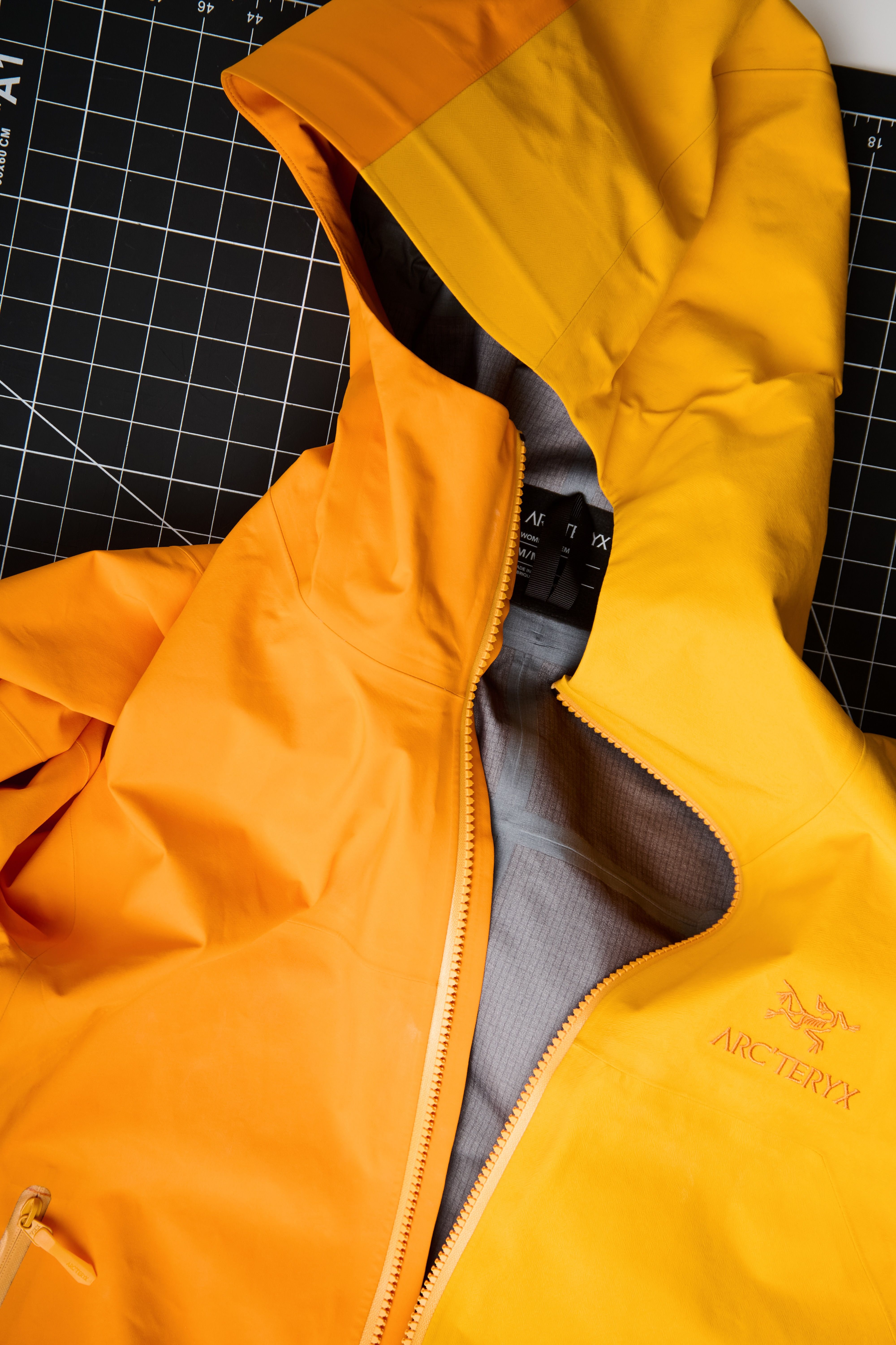 An orange and yellow Arc'teryx jacket, partially unzipped, on a black cutting mat.