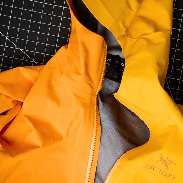 An orange and yellow Arc'teryx jacket, partially unzipped, on a black cutting mat.