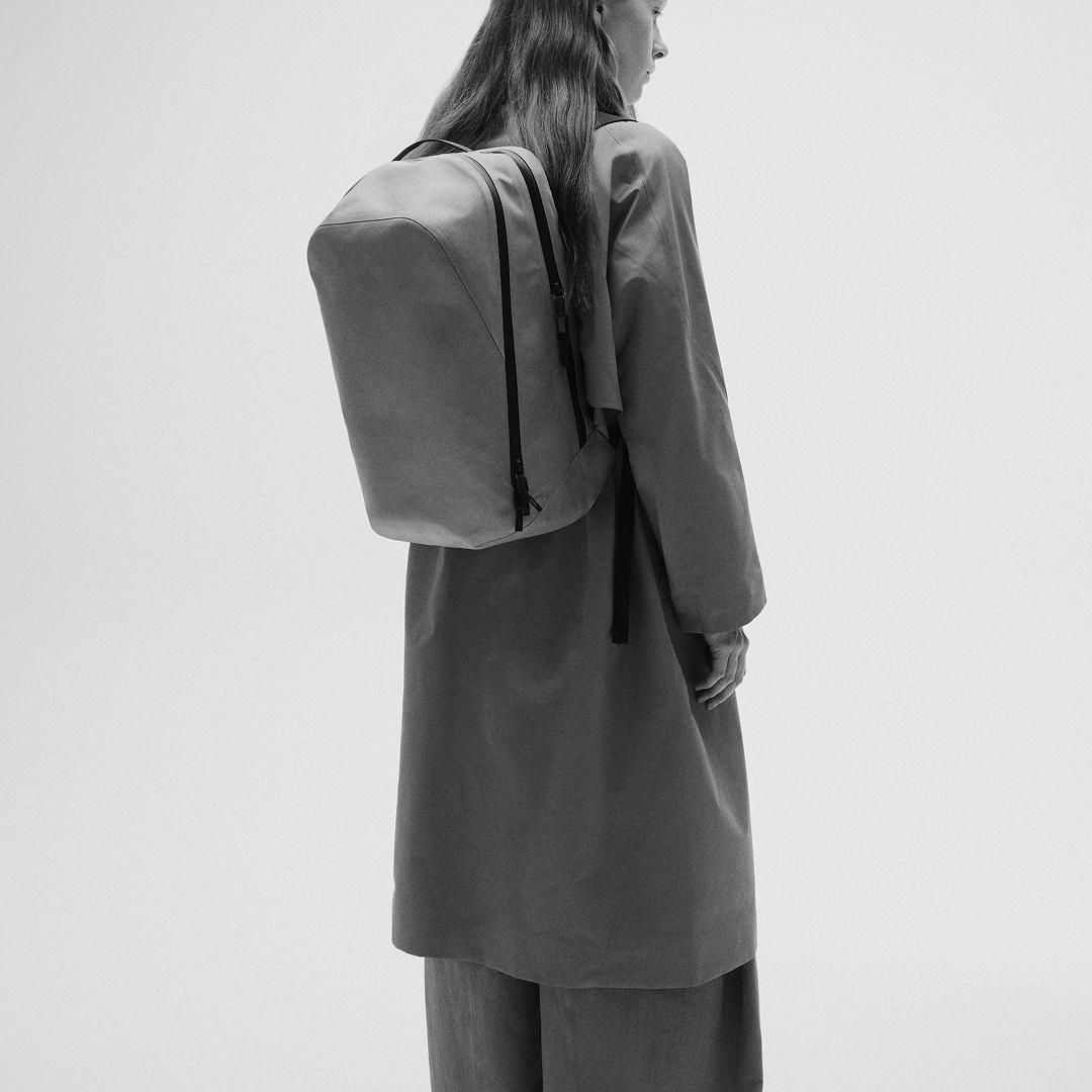 Black and white image of a person from behind wearing a minimalist backpack and long coat.