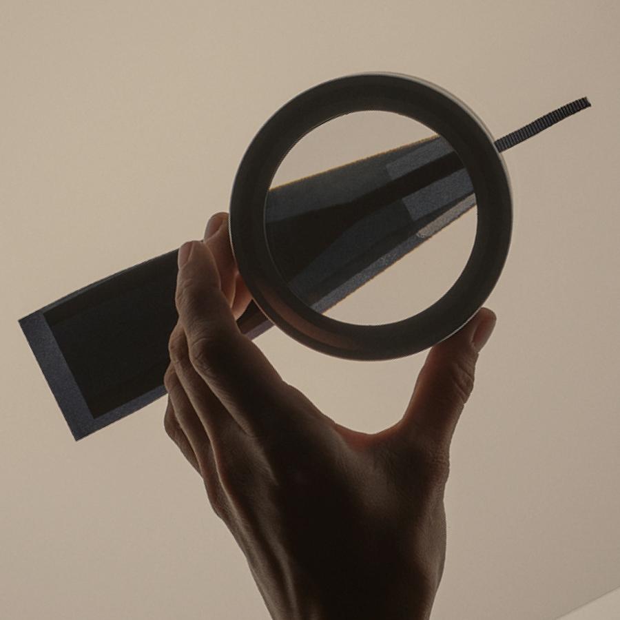 Silhouetted hand holding a magnifying glass examining a patterned dark ribbon.