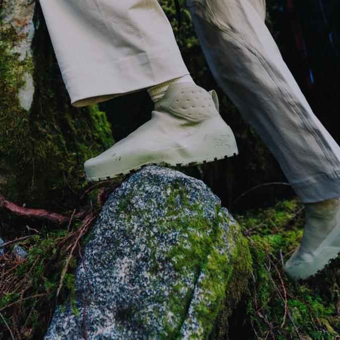 A light green high-top boot steps on a moss-covered rock.