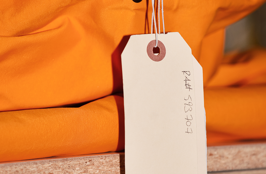 A beige tag with "R4## 593707" handwritten on it hangs from an orange fabric.
