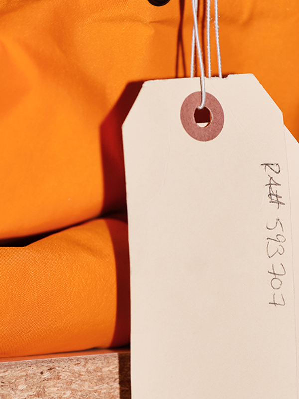 A beige tag with "R4## 593707" handwritten on it hangs from an orange fabric.