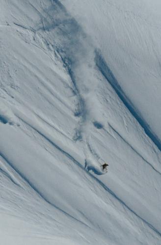 A skier descends a steep, snowy mountain, kicking up powder.