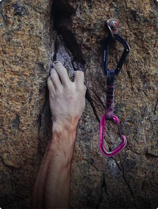 Climber's hand gripping a rock crack beside a quickdraw on a bolt.