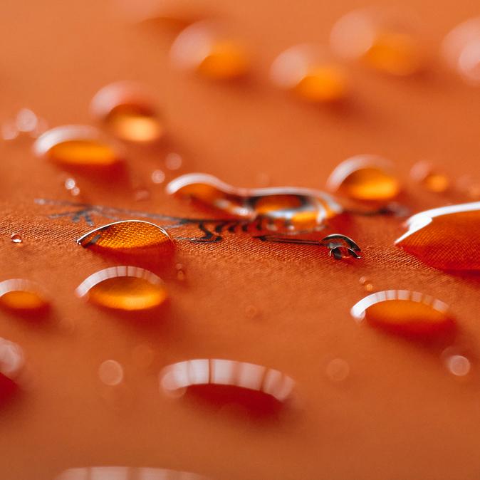 Close-up of water droplets beading on an orange, water-repellent fabric.