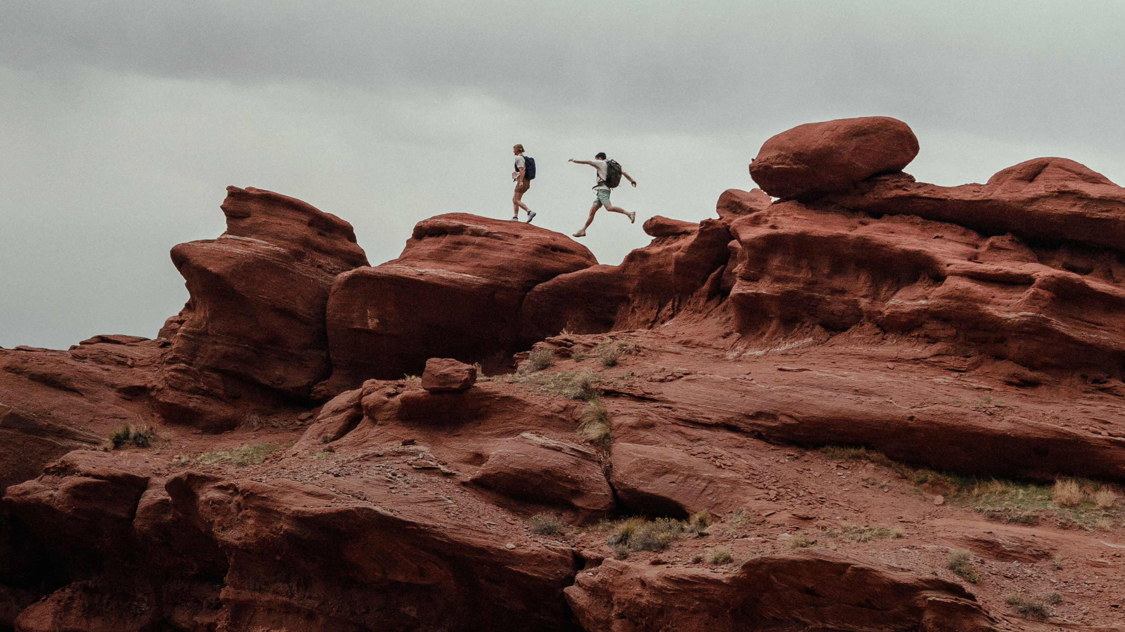 Two people hiking on red rock formations, one jumping.