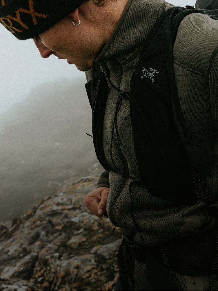 A hiker in Arc'teryx gear looks down on a rocky, misty mountain trail.