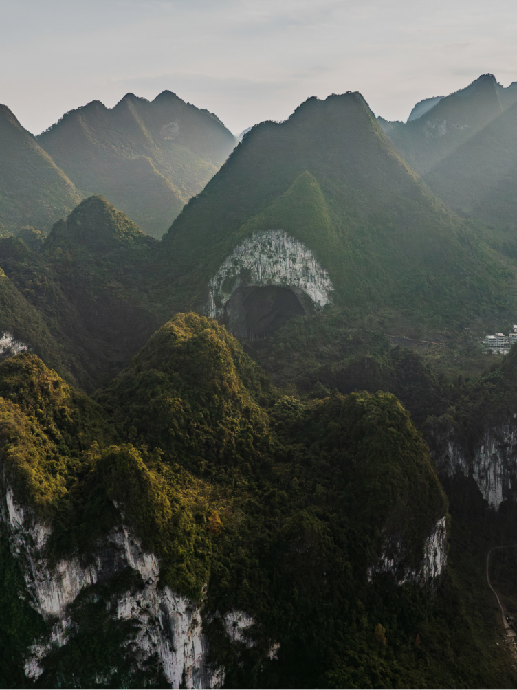 Lush green karst mountains with a massive arch-shaped cave.