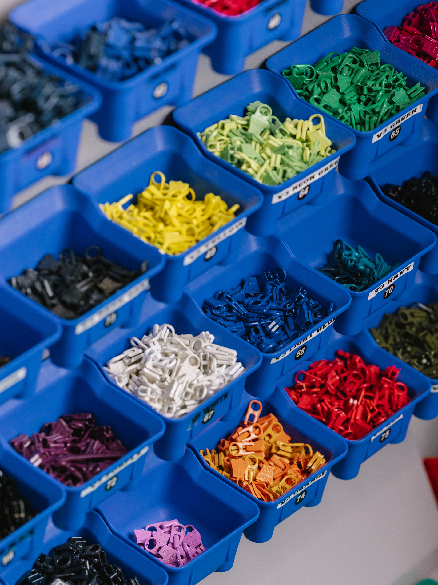 Numerous blue bins filled with colorful plastic zipper pulls, organized in rows.