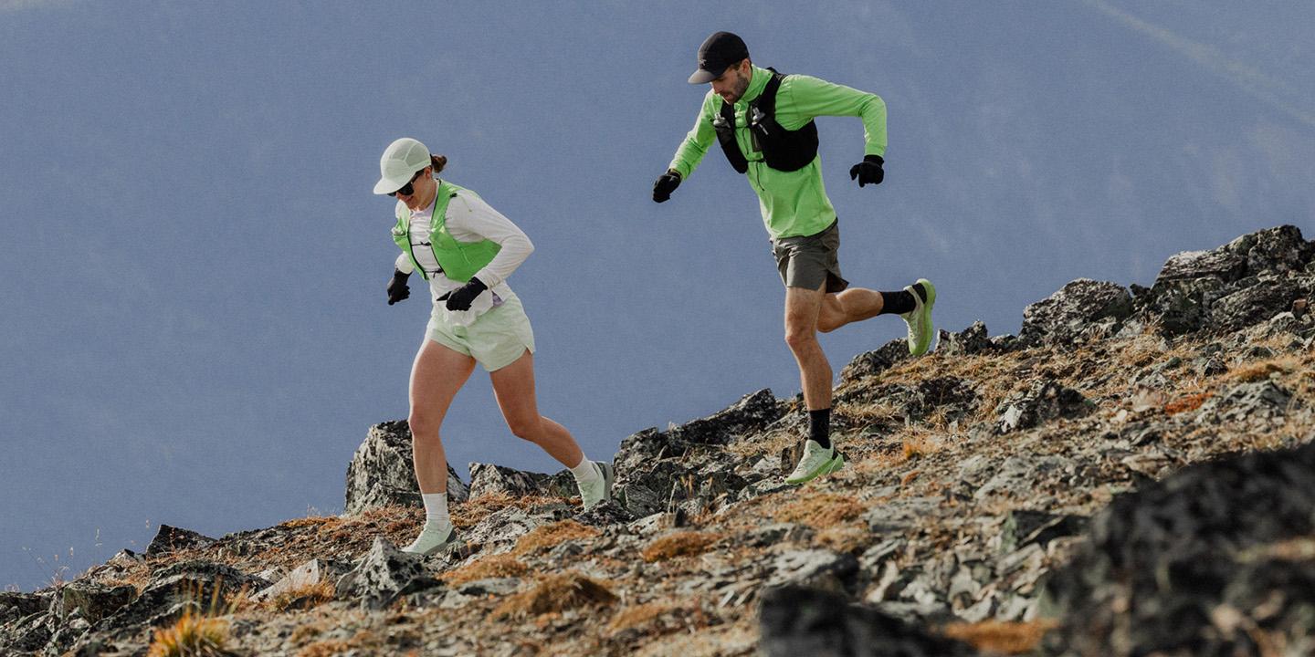 Two trail runners ascend a rocky mountain slope.