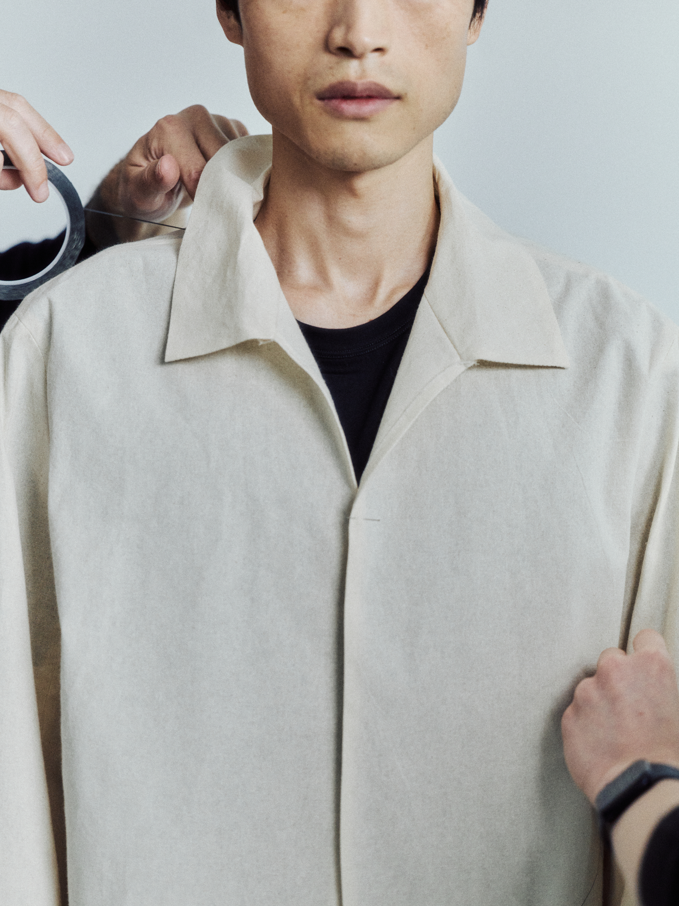A man in a light jacket is fitted, with hands adjusting his clothing and holding tape.