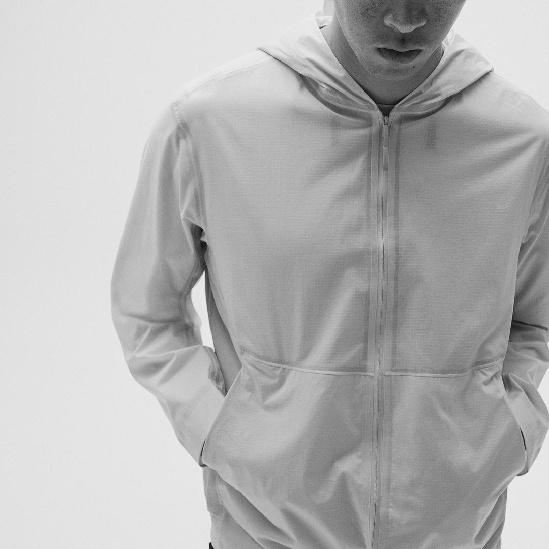 A person wearing a light grey hooded zip-up jacket with hands in pockets.