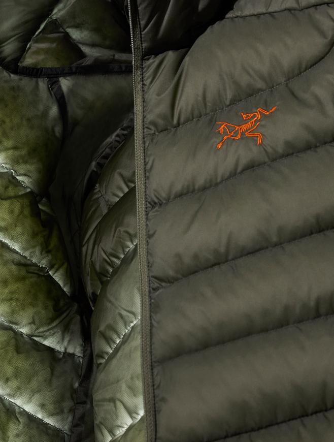 A close-up of an olive green puffer jacket with an orange Arc'teryx logo and a zipper.