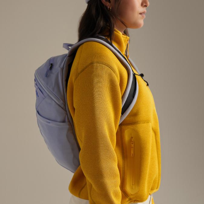 A person in profile wears a mustard yellow fleece jacket and a light purple backpack.