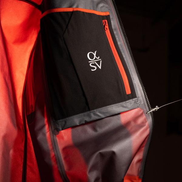 Interior of a technical jacket showing bright orange lining and a black internal pocket with an orange zipper and 'α SV' logo.