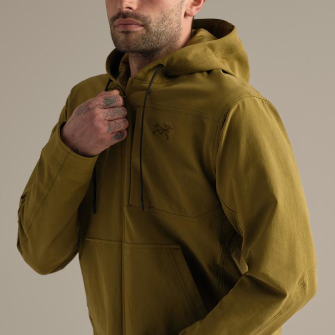 Man wearing an olive green Arc'teryx hooded anorak, adjusting the neck drawstring.