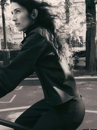 A woman wears a pink cropped jacket and black pants, looking right.