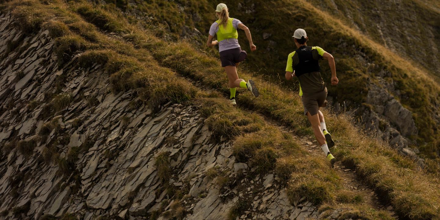 Two people trail running up a steep, grassy mountain trail.