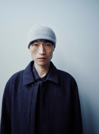 A man wearing a light gray beanie and dark wool jacket looks directly at the camera.