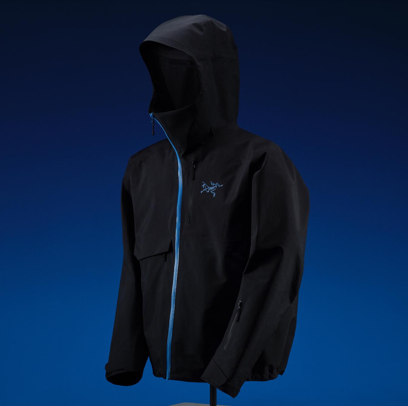 Black Arc'teryx jacket with a blue main zipper and logo, displayed on a stand against a blue background.